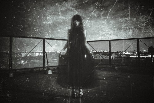 夜の屋上でフェンス前に立つ黒いドレスを着た女性の姿