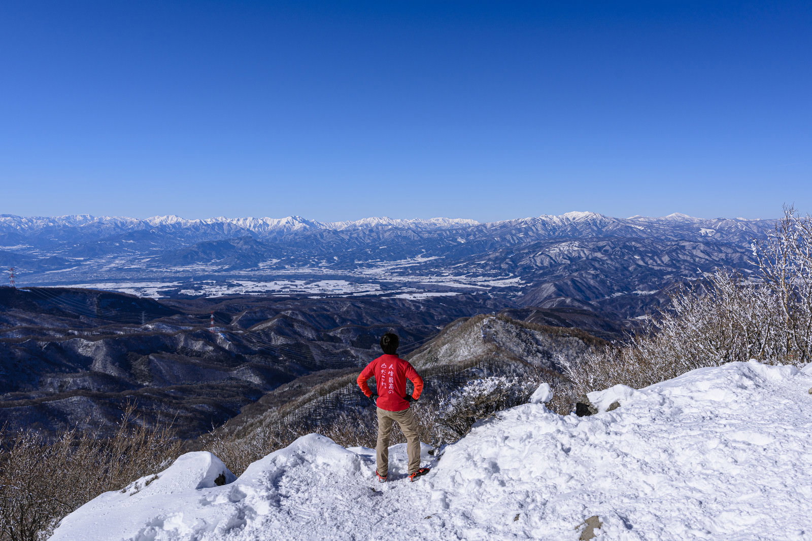 赤城山の雪山山頂で青空を背景に仁王立ちする赤いウェアの登山者