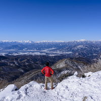 赤城山の雪山山頂で仁王立ちする赤いウェアの登山者の写真