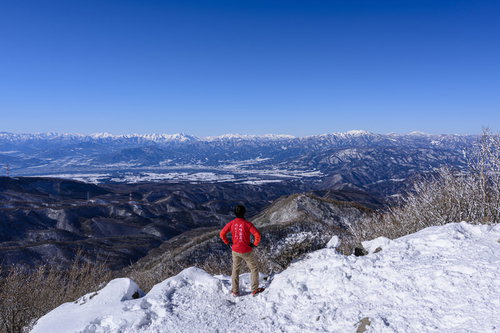 赤城山の雪山山頂で仁王立ちする赤いウェアの登山者