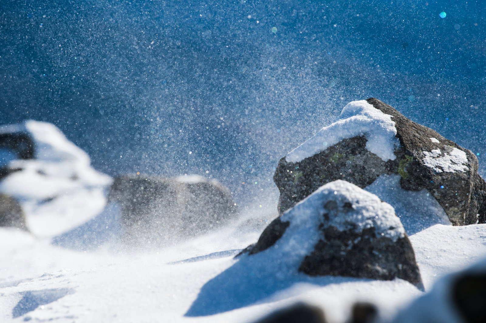雪に覆われた山の岩場で強風により舞い上がる雪の粒子