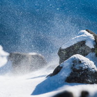厳冬期の蓼科山で舞い上がる雪の粒子と岩場の風景の写真