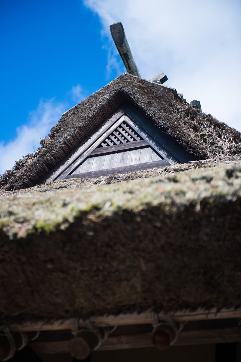 青空を背景にした茅葺屋根の古民家を下から見上げたアングル