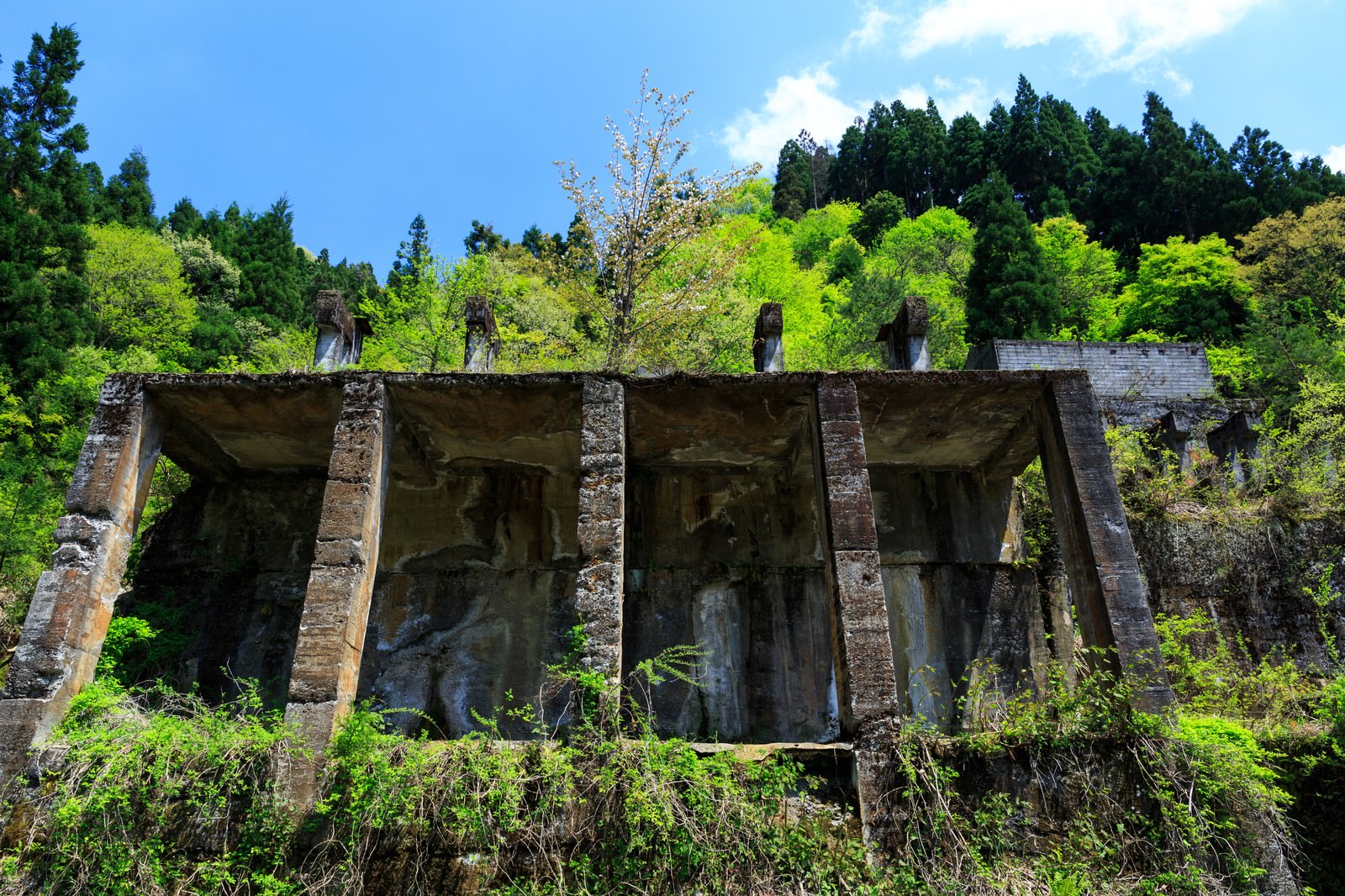 青空の下、緑豊かな山間にある土倉鉱山跡のコンクリート廃墟