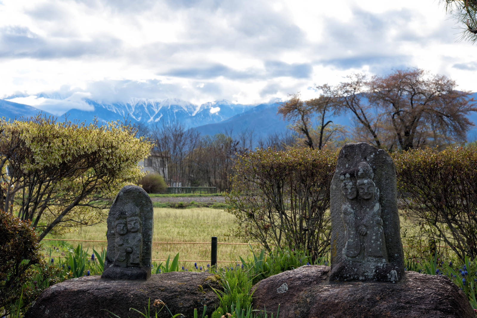 山々を背景に佇む安曇野市の道祖神の石仏