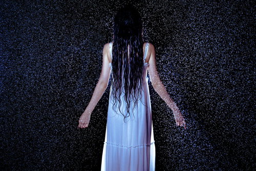 激しい雨に打たれてびしょ濡れになる白いワンピース姿の女性