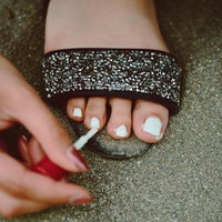 足の指に白いマニキュアを塗る（ビジューサンダル）の写真