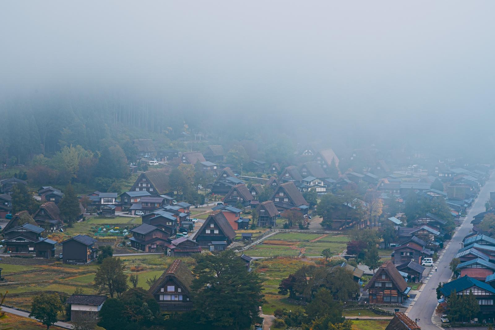 白川郷の合掌集落を覆う朝霧の中に、茅葺屋根の家々が立ち並ぶ風景