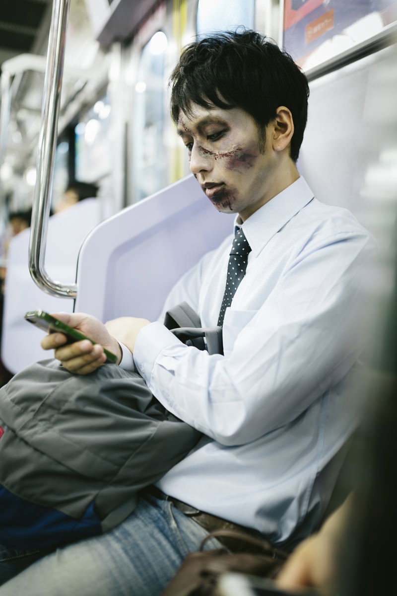 傷跡のある顔で電車内で携帯端末を握る白シャツの男性［モデル：大川竜弥］