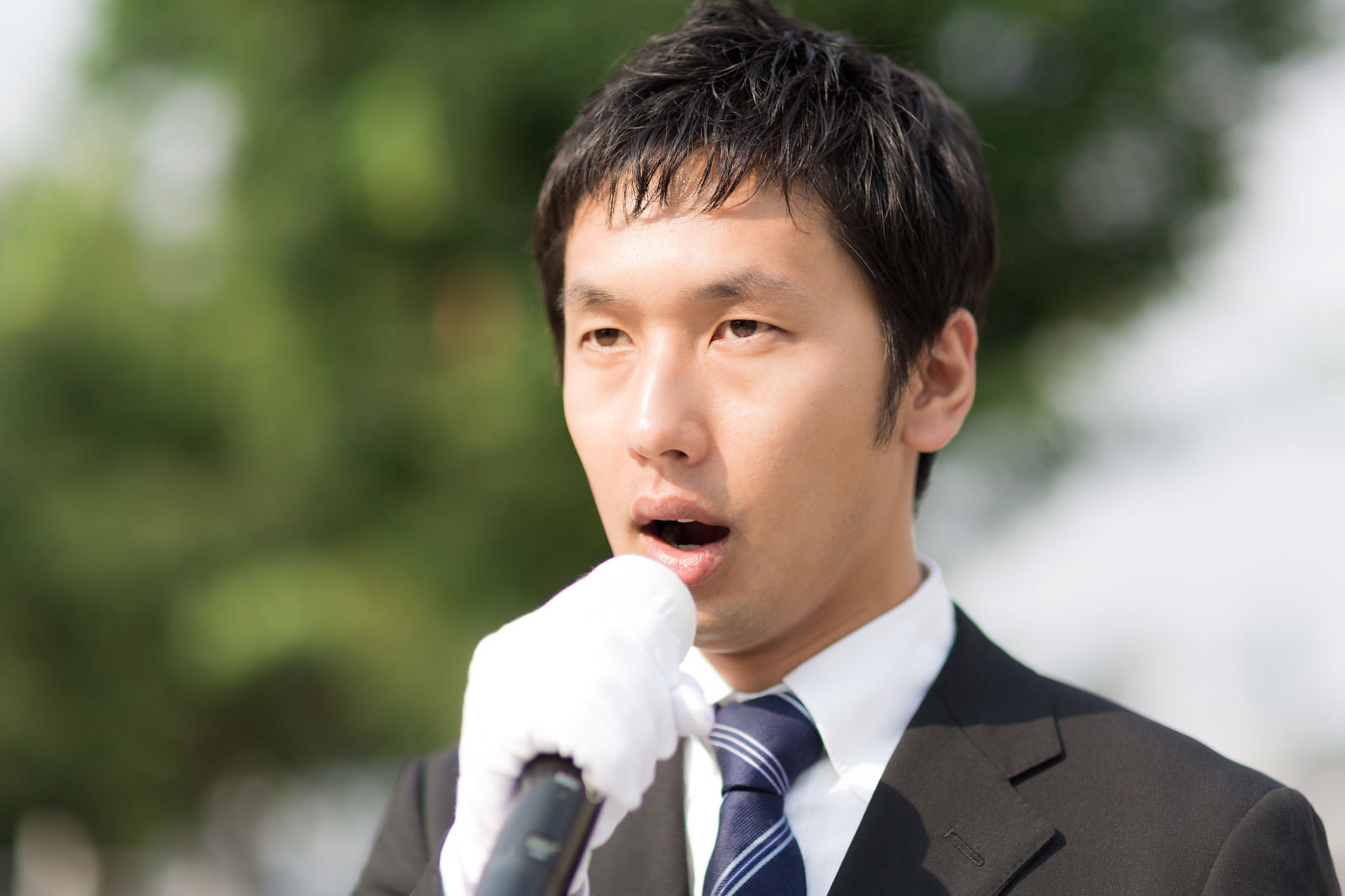 スーツ姿の男性がマイクを持って街頭演説している［モデル：大川竜弥］