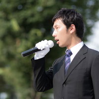 街頭演説でマイクを握り政策を訴える若手議員の写真