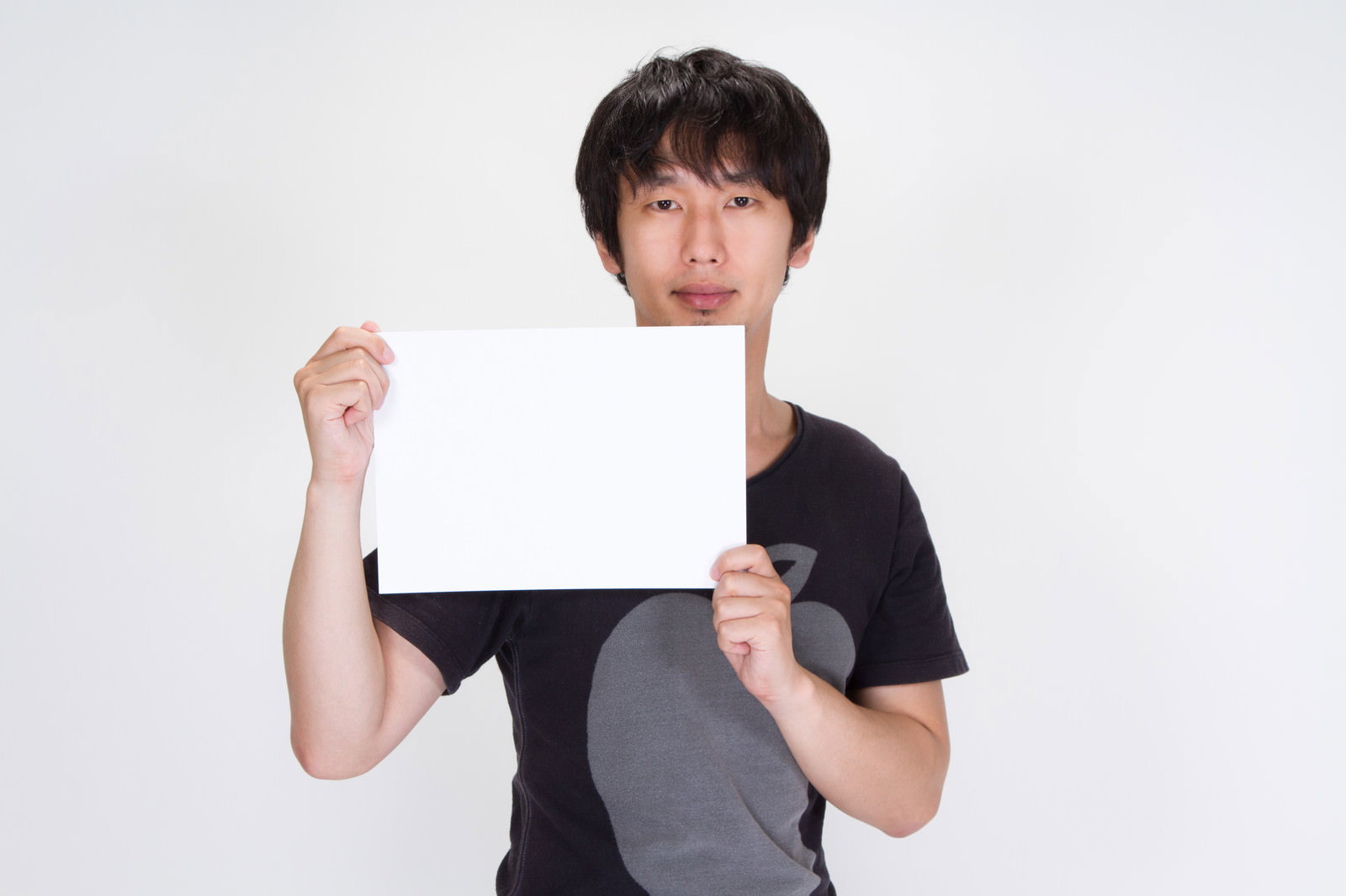 白い紙を両手で掲げる黒Tシャツの男性［モデル：大川竜弥］