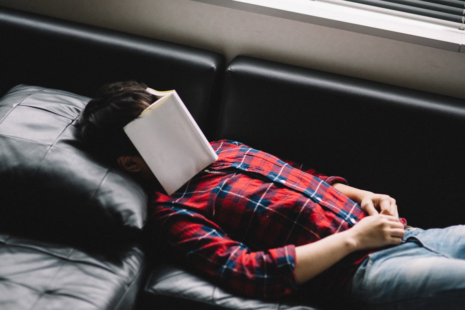 黒いソファで技術書を顔に乗せて寝る男性［モデル：大川竜弥］