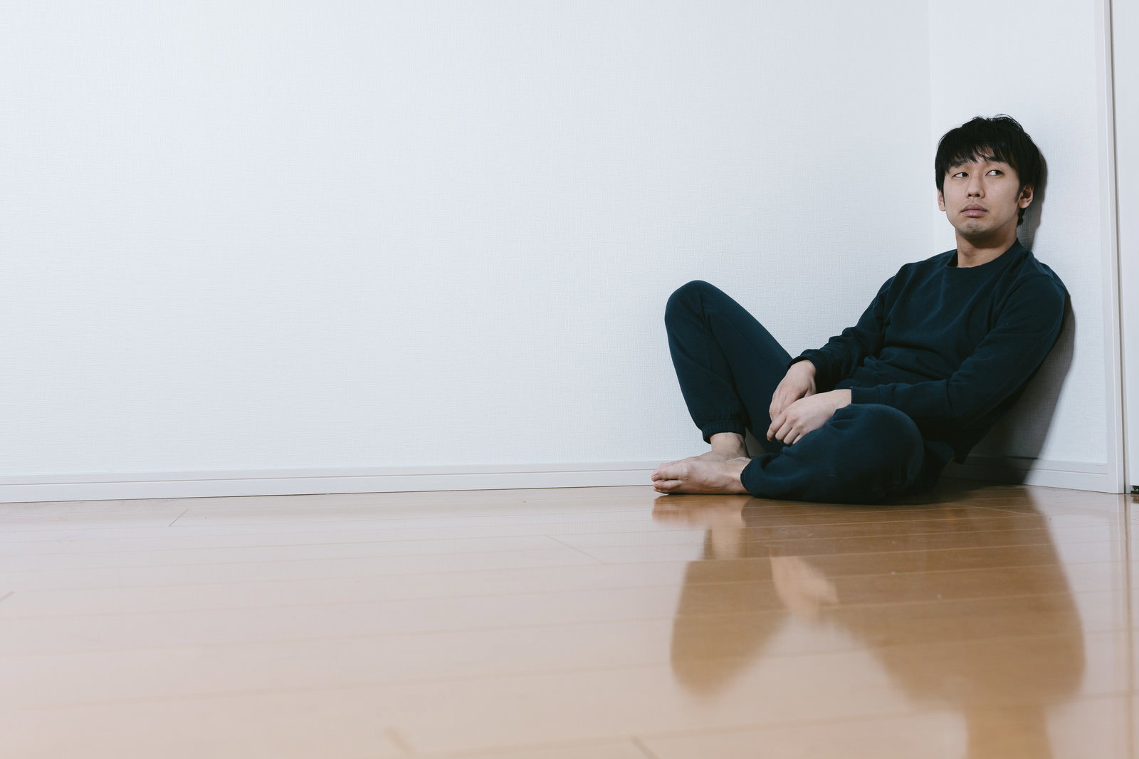 床に座り斜め上を見つめる男性［モデル：大川竜弥］