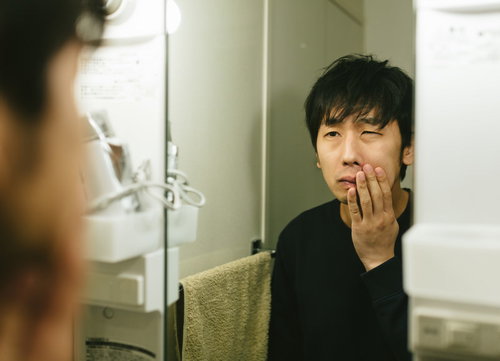 洗面台の鏡を見つめてカミソリ負けに悩む男性