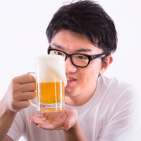 泡が溢れる生ビールをグラスに注ぐ黒縁眼鏡の男性の写真