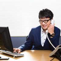 電話応対する若い営業男性がデスクでコンピューター操作の写真