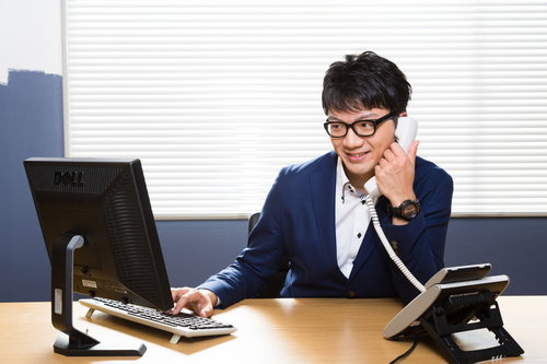 電話応対する若い営業男性がデスクでコンピューター操作