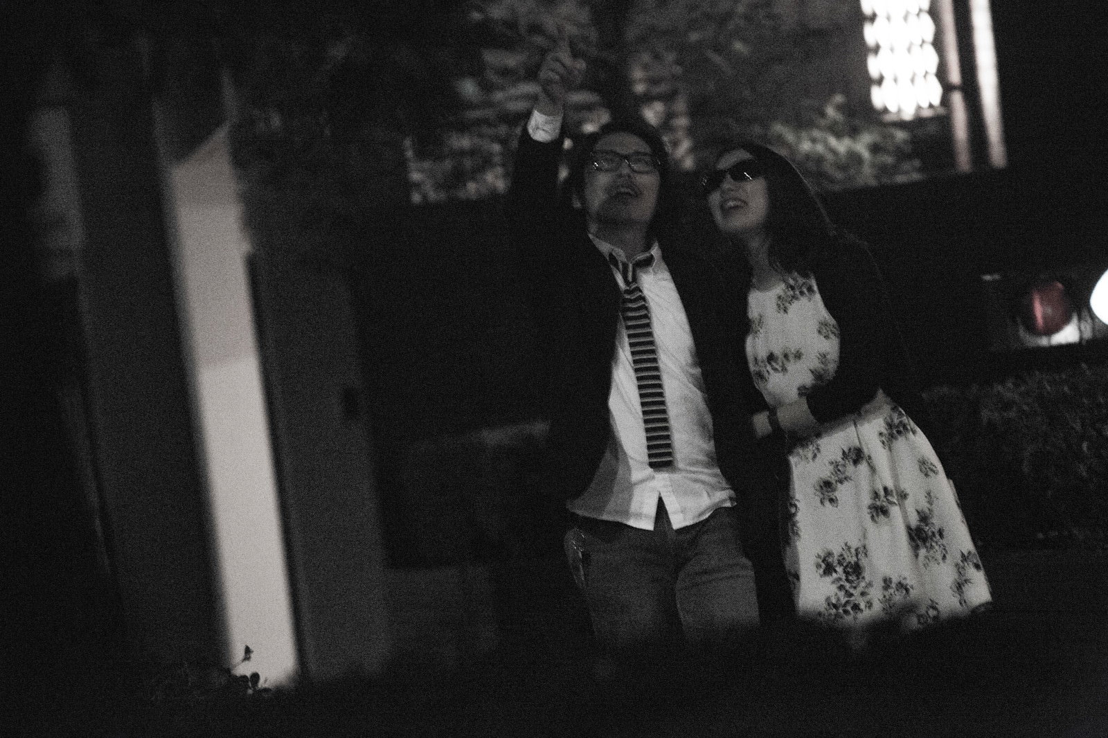 夜の街中で男性が指さしながら女性に話しかける白黒写真［モデル：ゆうせい］