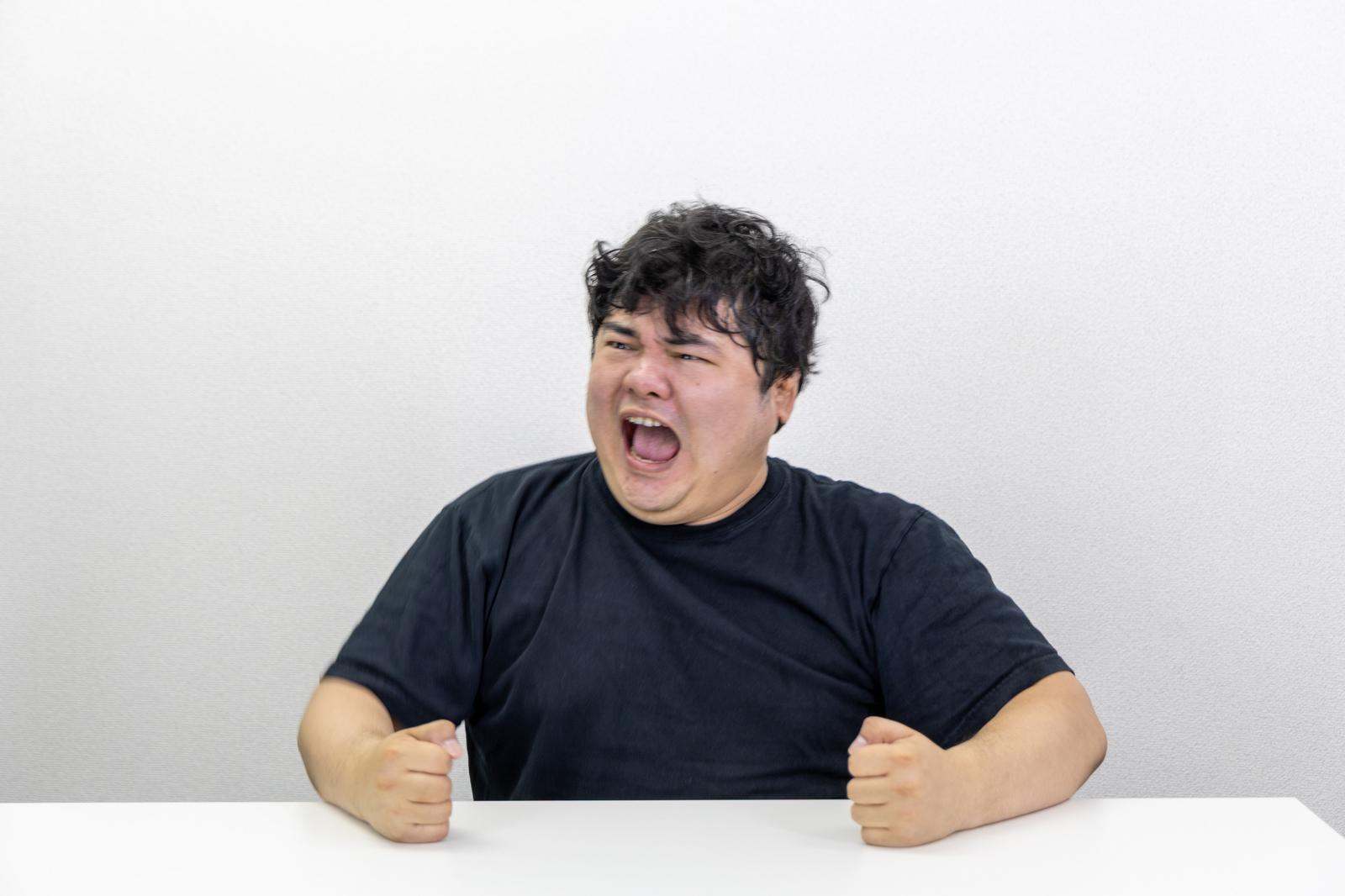 机を叩いて怒る男性。黒いTシャツを着て上を向いて叫んでいる［モデル：段田隼人］