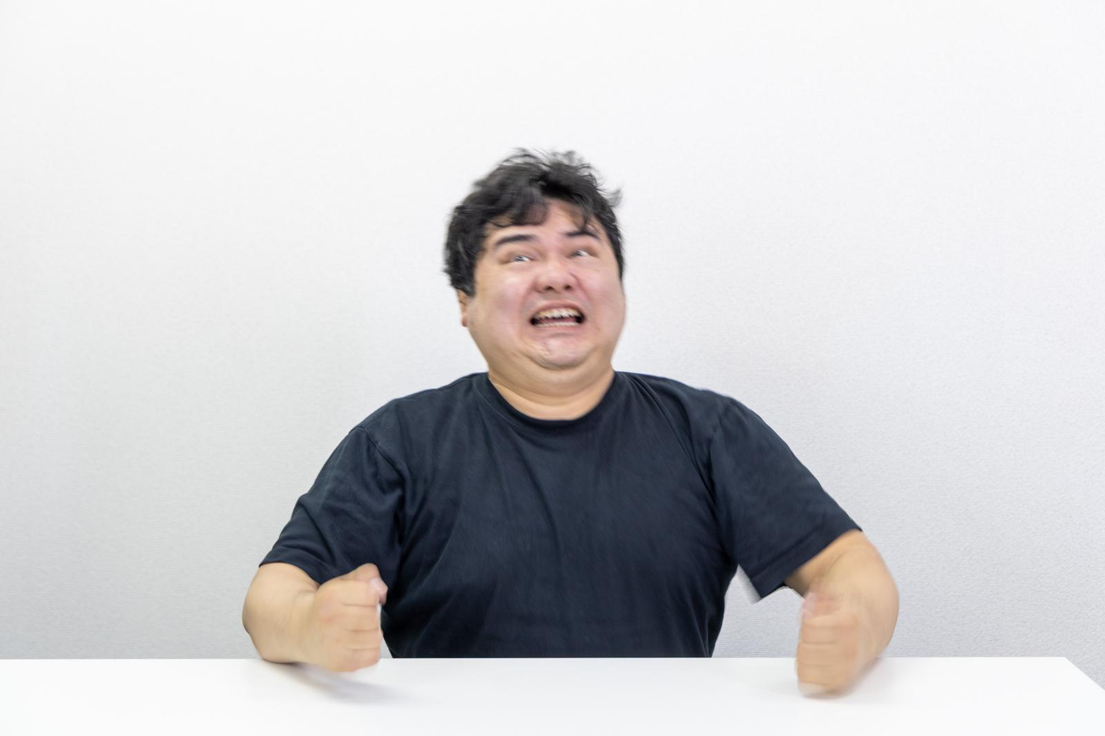 無念な表情で机を叩く男性が歯を食いしばっている［モデル：段田隼人］