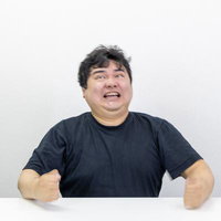 無念の表情で歯を食いしばり机を叩く黒いTシャツの男性の写真