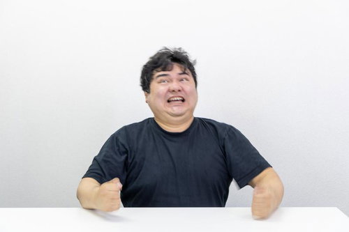 無念の表情で歯を食いしばり机を叩く黒いTシャツの男性