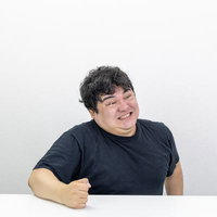 黒Tシャツ姿で歯を食いしばり台パンする男性の写真