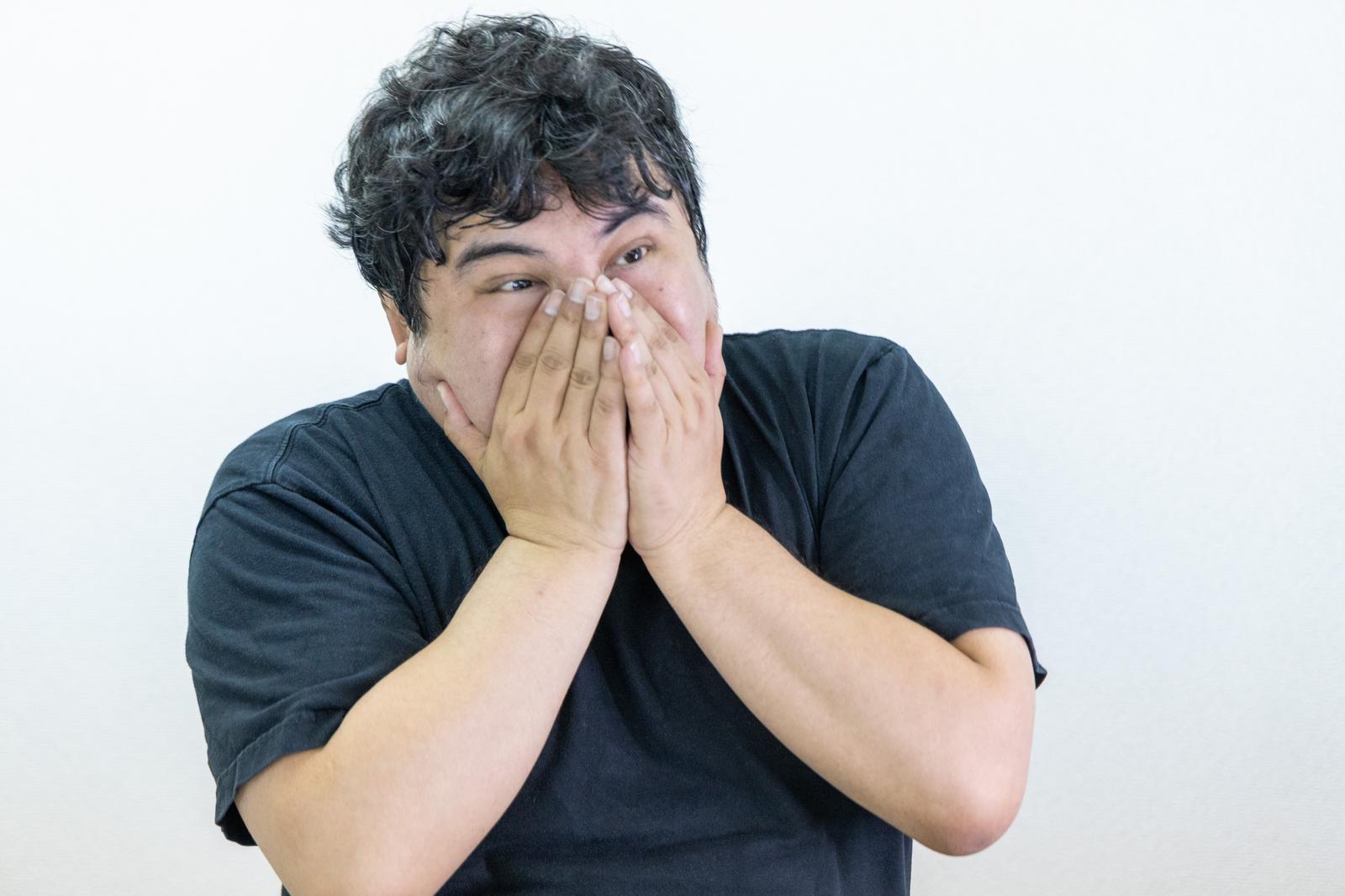 両手で口元を覆い隠している黒Tシャツの日本人男性［モデル：段田隼人］