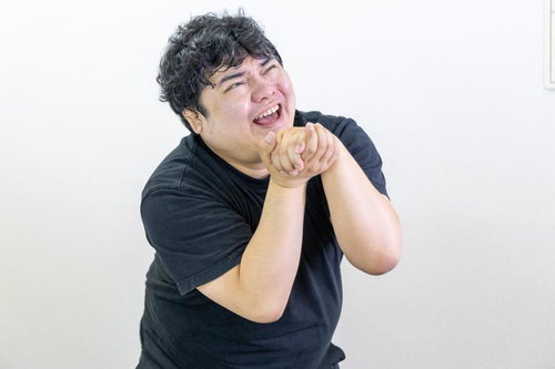 黒いTシャツの男性が両手を合わせて媚びへつらう表情のポートレート