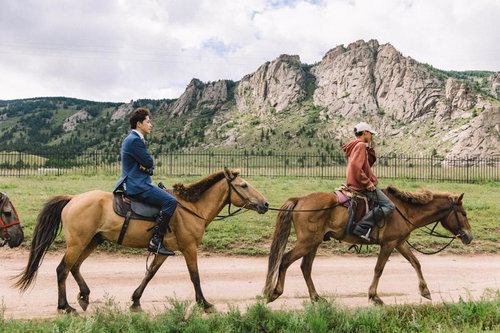 モンゴルの草原を馬で行くスーツ姿のビジネスマン