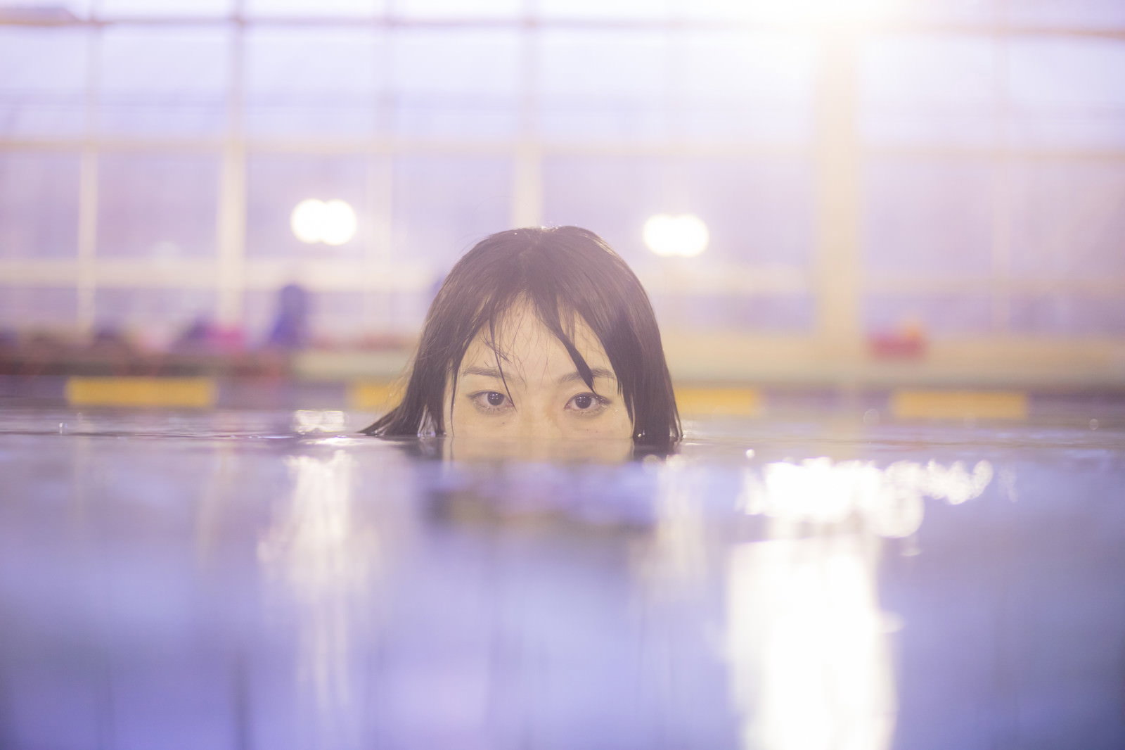 薄暗い屋内プールで水面から顔を出し、鋭い視線を向ける女性［モデル：たけべともこ］