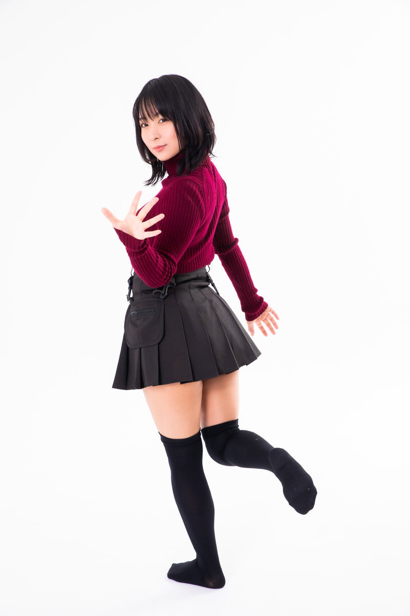振り返ってバイバイする赤い上着とグレーのスカートの女性［モデル：にゃるる］