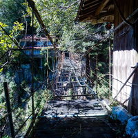 廃墟となった旅館へ続くボロボロの木造吊り橋の写真