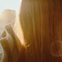 夕陽があたる女性の後ろ姿と長い髪、黄金色に輝くロングヘアの写真