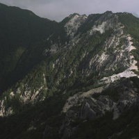 白い露岩が輝く日差しの鳳凰三山の山肌と針葉樹林の写真