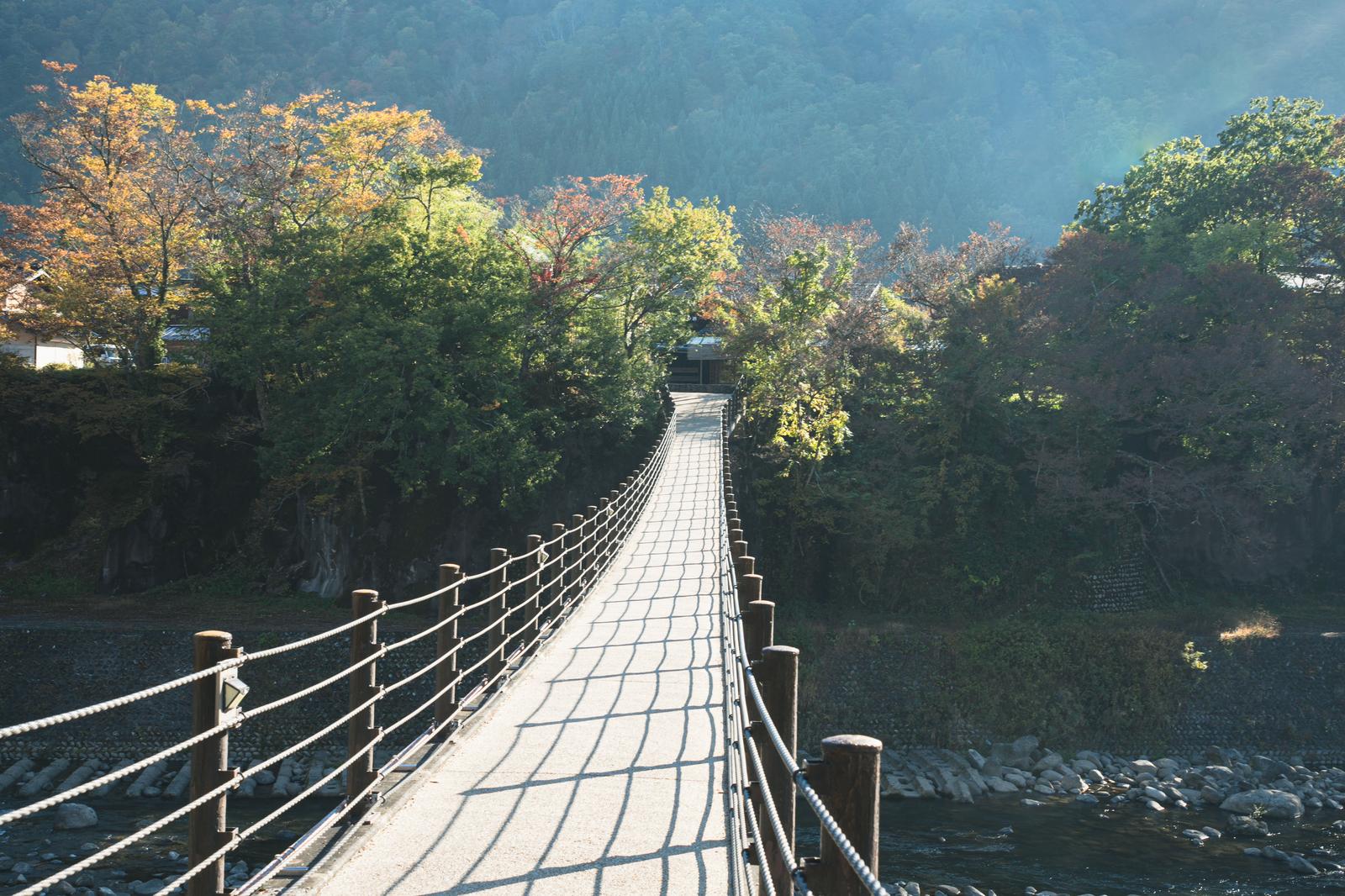 秋の樹木に囲まれた白川郷のであい橋が山間の谷を横断する風景