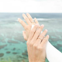 海をバックに重ねた手とペアリングの写真