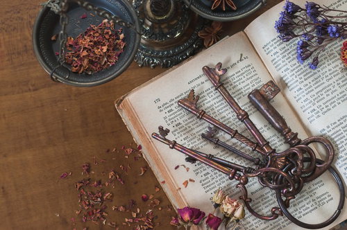 木製テーブルに並べた古い鍵と古書、紫色のドライフラワー