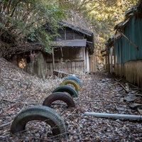 廃校の校舎裏に放置された古タイヤと風化した建物の写真