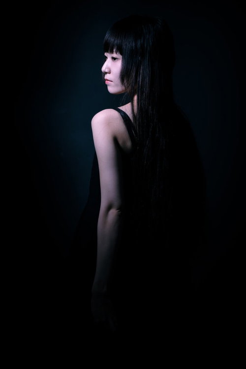 黒い暗がりに浮かぶ半身の女性の後ろ姿