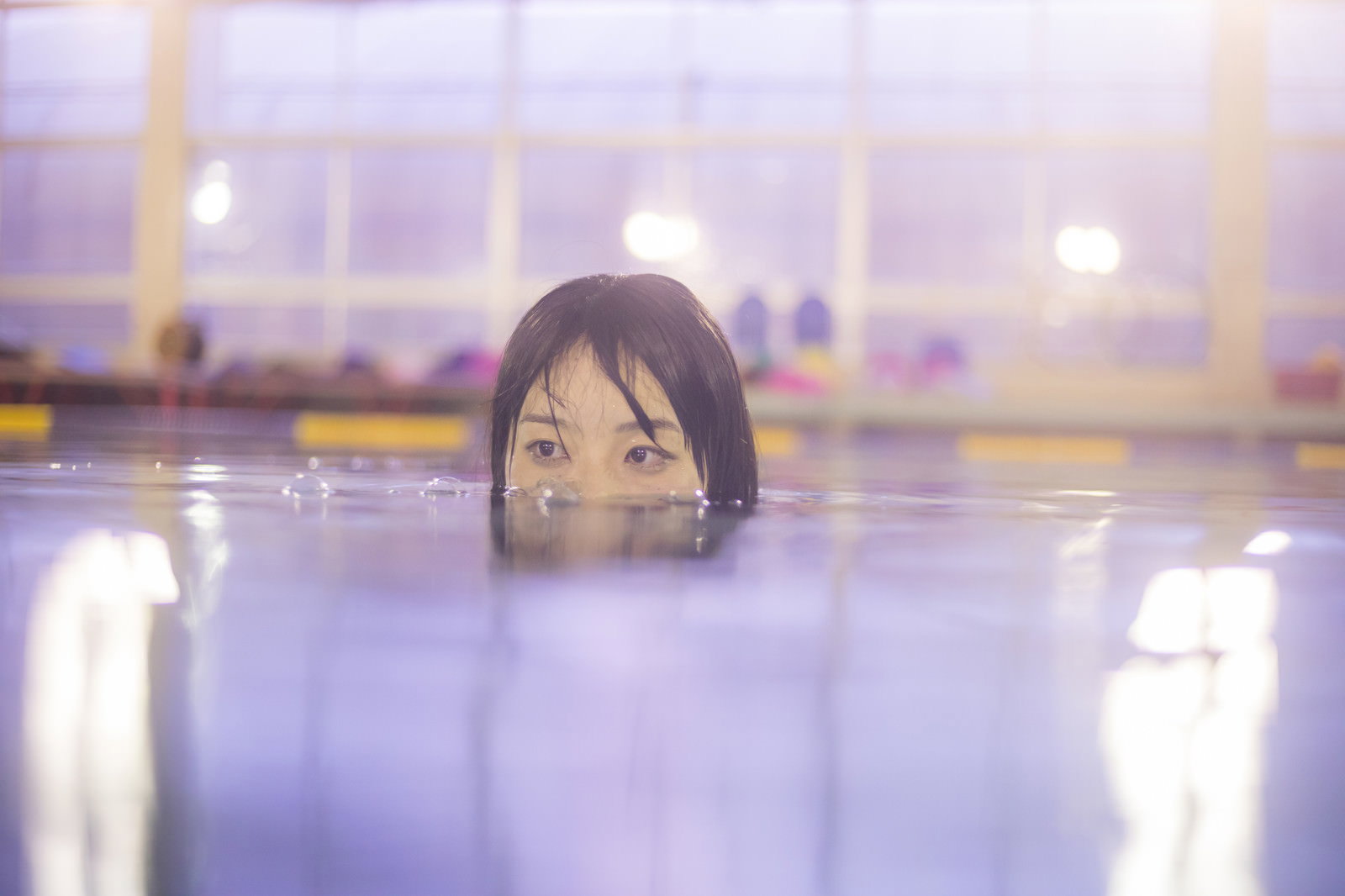 プールの水面から目元だけを出して覗いている女性［モデル：たけべともこ］