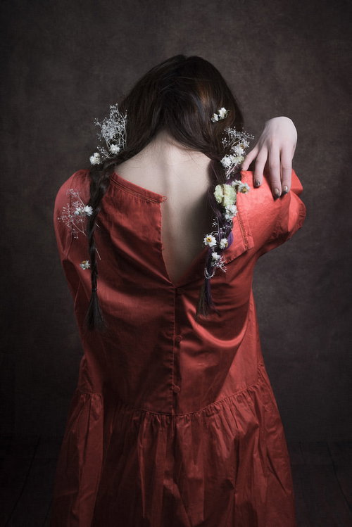 赤いドレスの背中ファスナーに手を伸ばす三編みの女性モデル