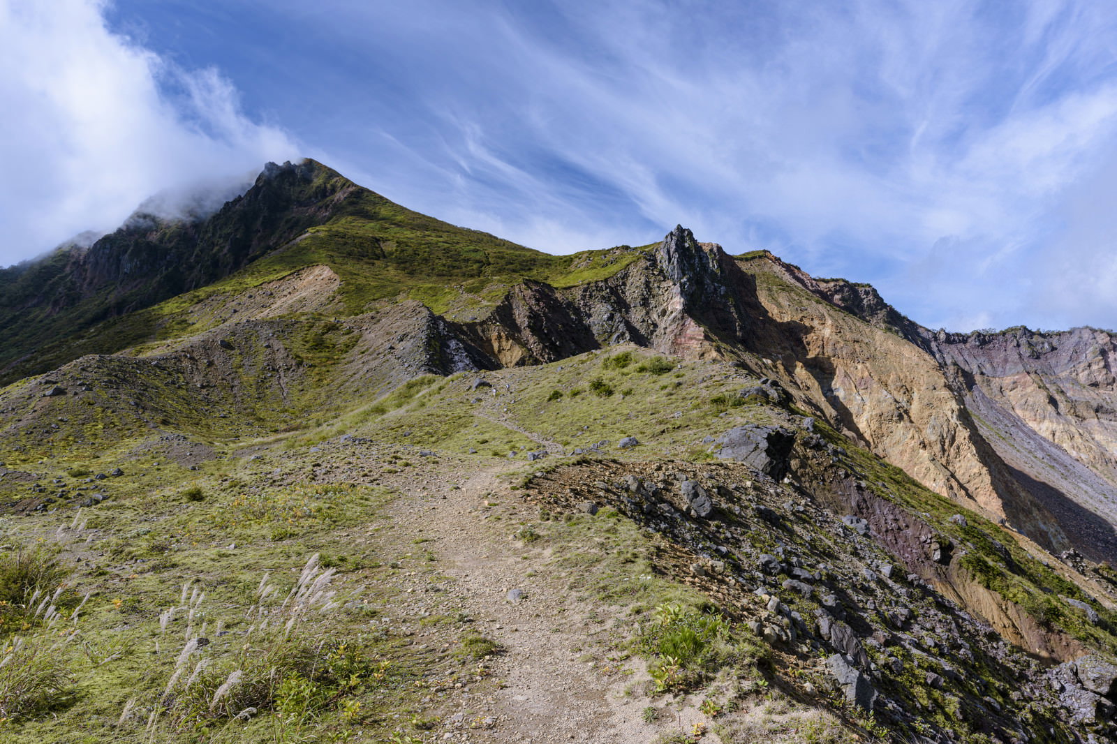 火山特有の荒々しい崖と緑の斜面が広がる磐梯山の登山道風景