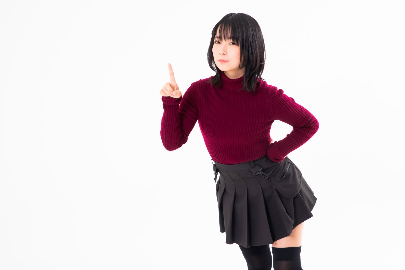 エンジ色のニットを着た女性が右手の人差し指を上に向けるポーズ［モデル：にゃるる］