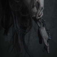 暗い背景で伸ばした指先と黒い髪の毛が絡みつく女性の手の写真