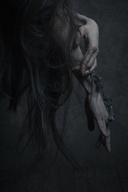 暗い背景で伸ばした指先と黒い髪の毛が絡みつく女性の手