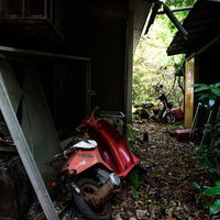 捨てられた赤いバイクと朽ちた廃屋の風景、錆び付いた原付の写真