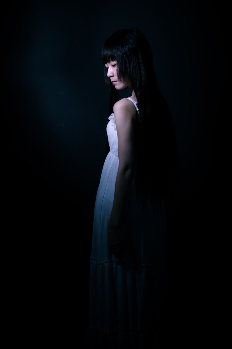 暗い背景の中に立つ女性の後ろ姿のシルエット［モデル：緋真煉］