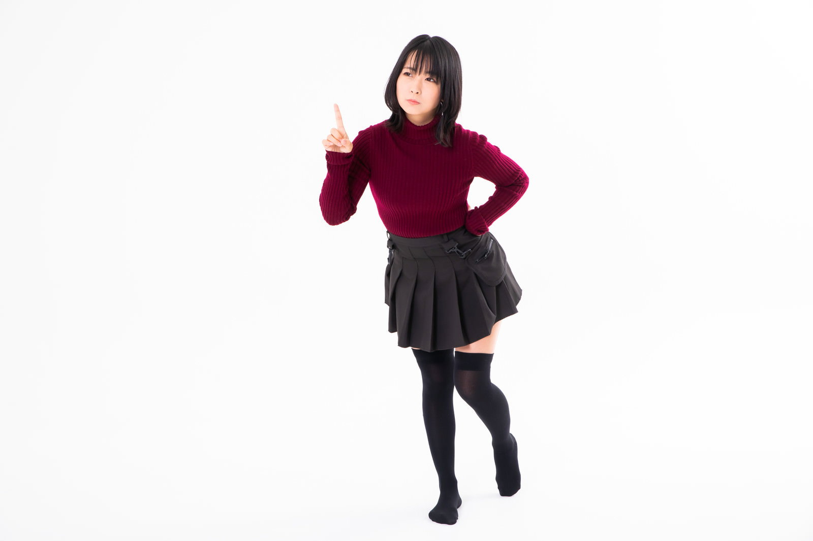 赤いトップスと黒いスカートを着た女性が人差し指を上に向けてポーズしている［モデル：にゃるる］